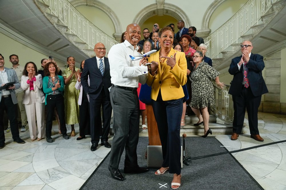 New York City Mayor Eric Adams and City Council Speaker Adrienne Adams stand together at City Hall holding a tiny toy plane.