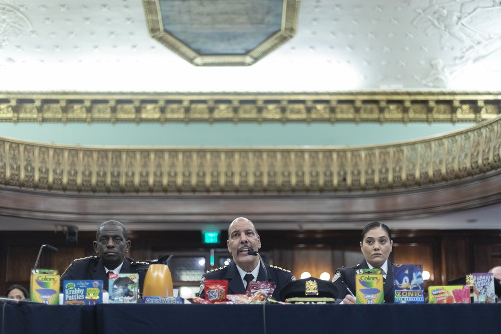 Sheriff Anthony Miranda sit at the center of a table flanked by two deputies. shows off illicit marijuana products.