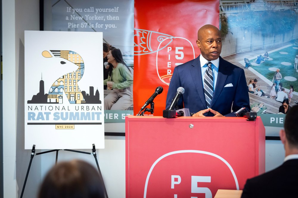 New York City Mayor Eric Adams stands next to a poster that says "National Urban Rat Summit."