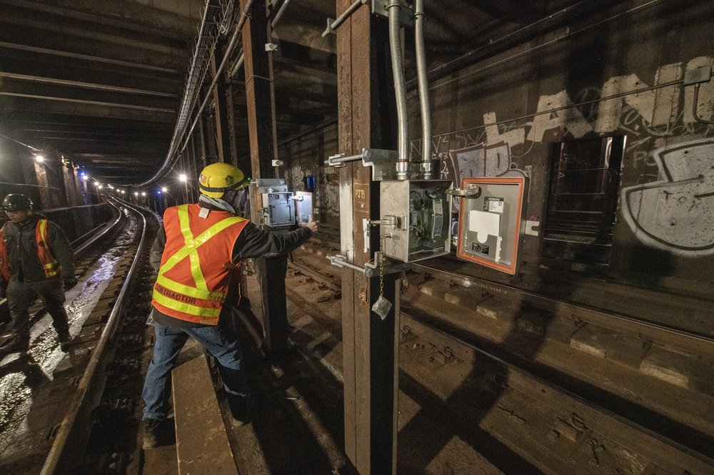 Crews in orange vests work on subway equipment in a tunnel.