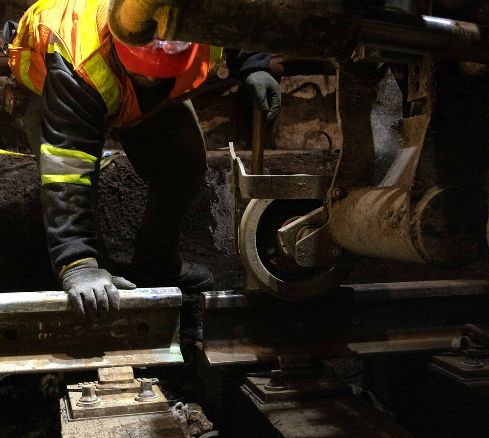 A worker manually guides a section of rail into place, preparing it to be secured onto the newly installed track ties, the Port Authority says.