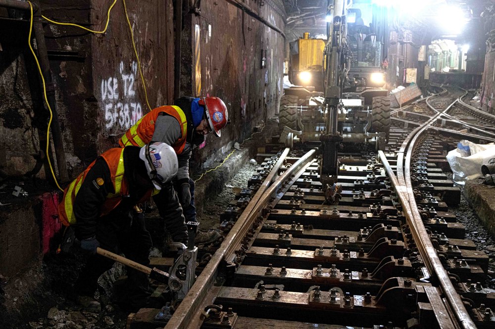 Workers use a track jack to lock new rail into place on top of newly laid ties. Behind them, elements of the station’s intricate interlocking system are visible, the Port Authority says.