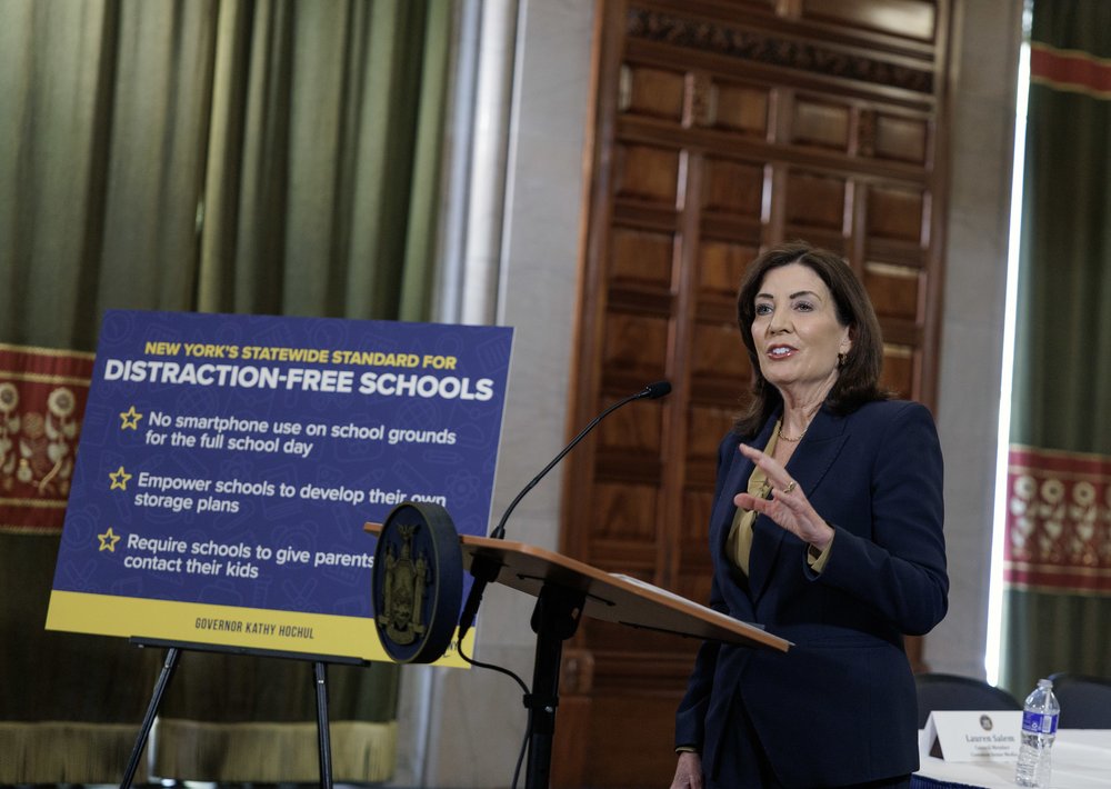 Gov. Kathy Hochul in front of a poster that reads Distraction-free schools