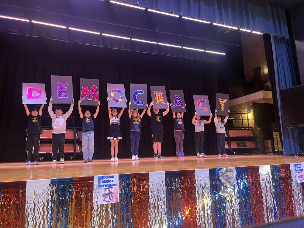 Students hold up a "democracy" sign on a stage.