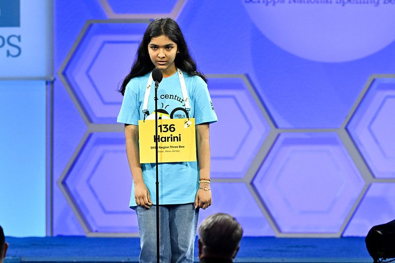 A girl stands on the stage and wears a sign that says "Harini."