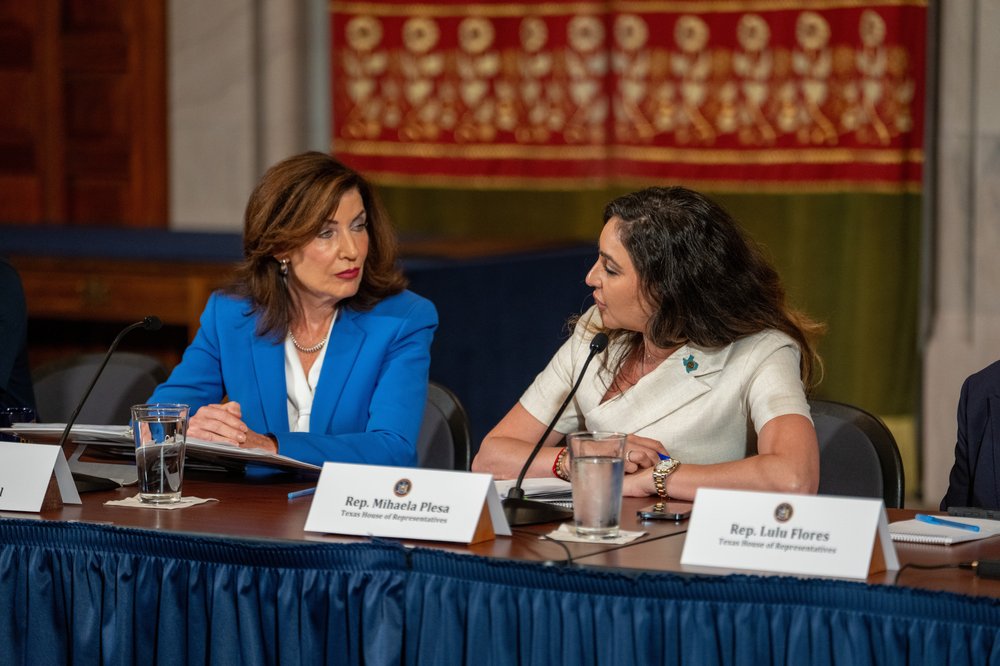 Gov. Hochul speaks to a woman wearing a white dress at a table.