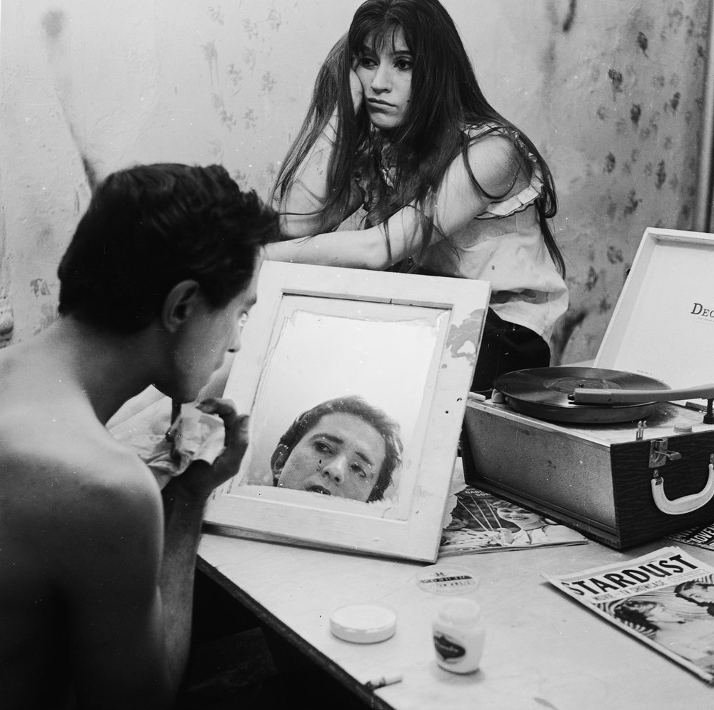 5efe4af78.jpeg "American sculptor and pop artist Claes Oldenburg makes himself up for a performance in Greenwich Village. He is a pioneer of the expressionist theatre known as 'Happening.' His wife Pat watches the proceedings with a bored expression. June 1962."