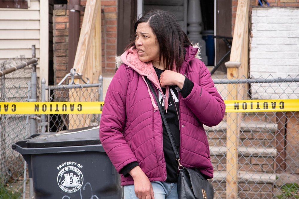 A woman stands in front of her home, which is blocked off with emergency tape.