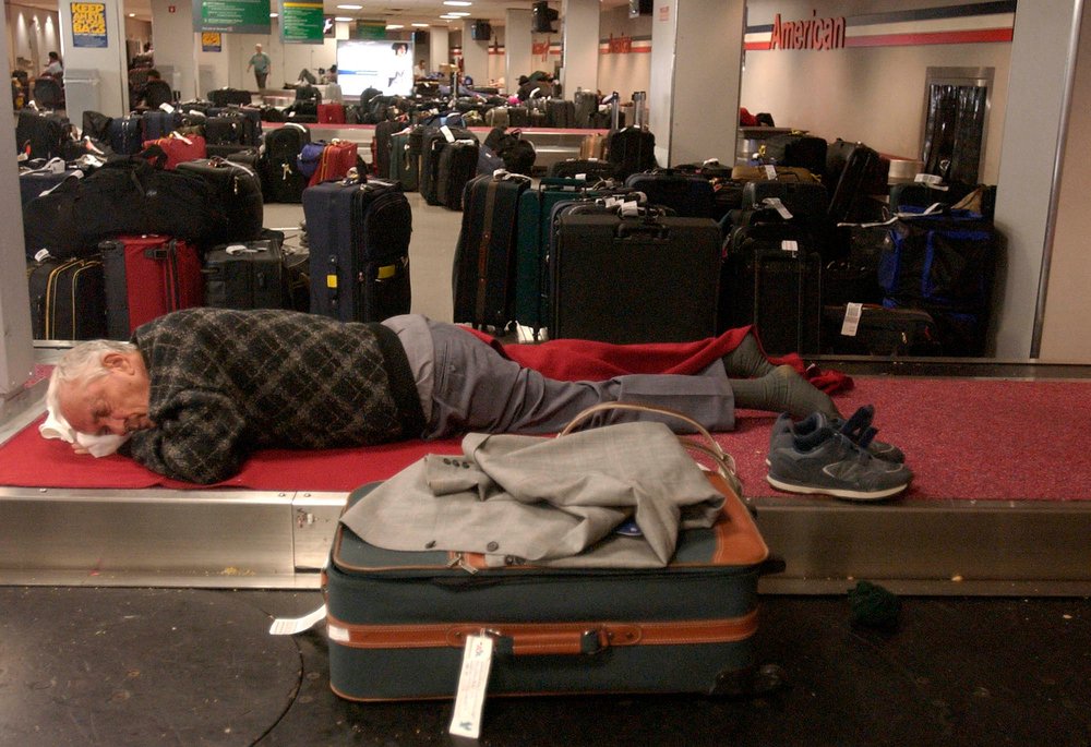 A stranded passenger sleeps on the luggage area at JFK Airport (Julie Jacobson/AP/Shutterstock)