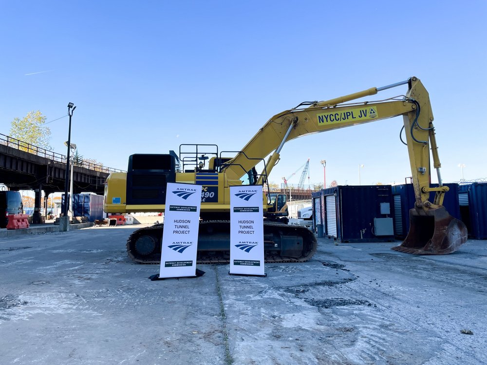 An excavator at a job site by signs reading "Hudson Tunnel Project."