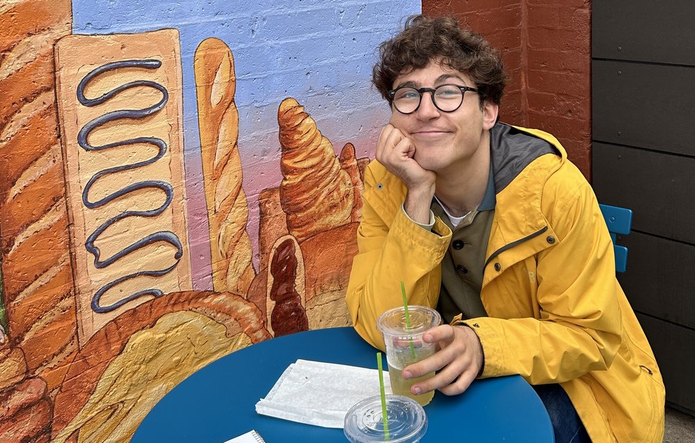 A man sits at a table wearing a yellow jacket.