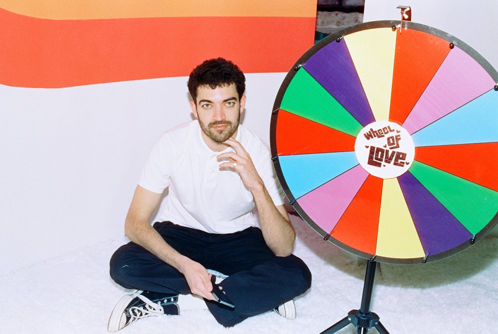 A man sits cross legged in front of a color wheel.