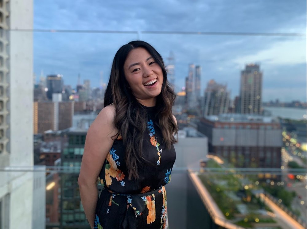 A woman poses on a balcony with skyscrapers in the background.
