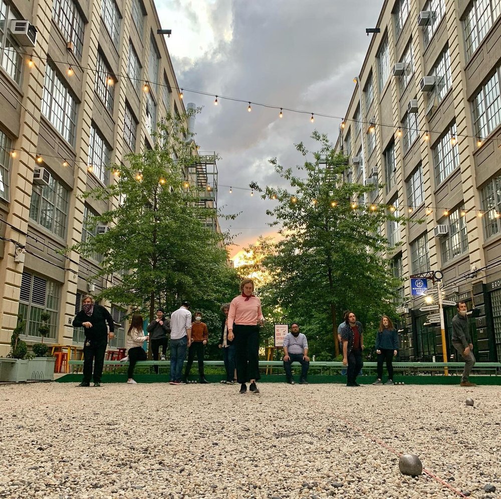 a Woman in a pink shirt stands on gravel and looks at her ball