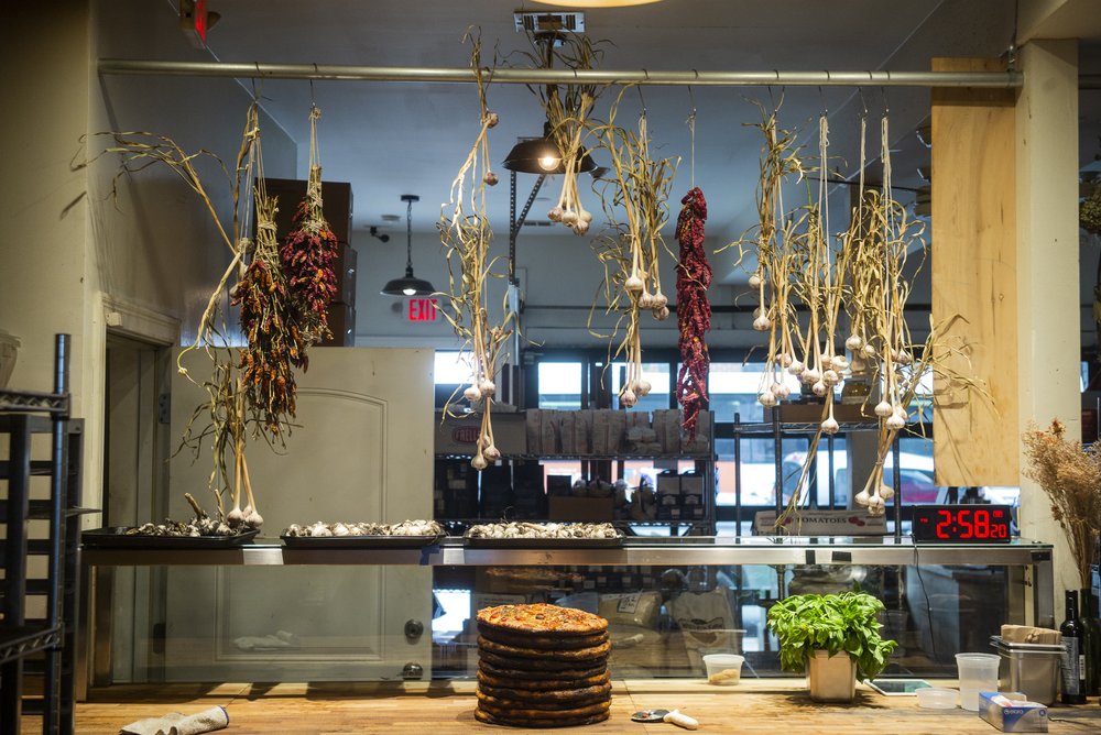 A stack of pizza pies on a counter with dried vegetables hanging above