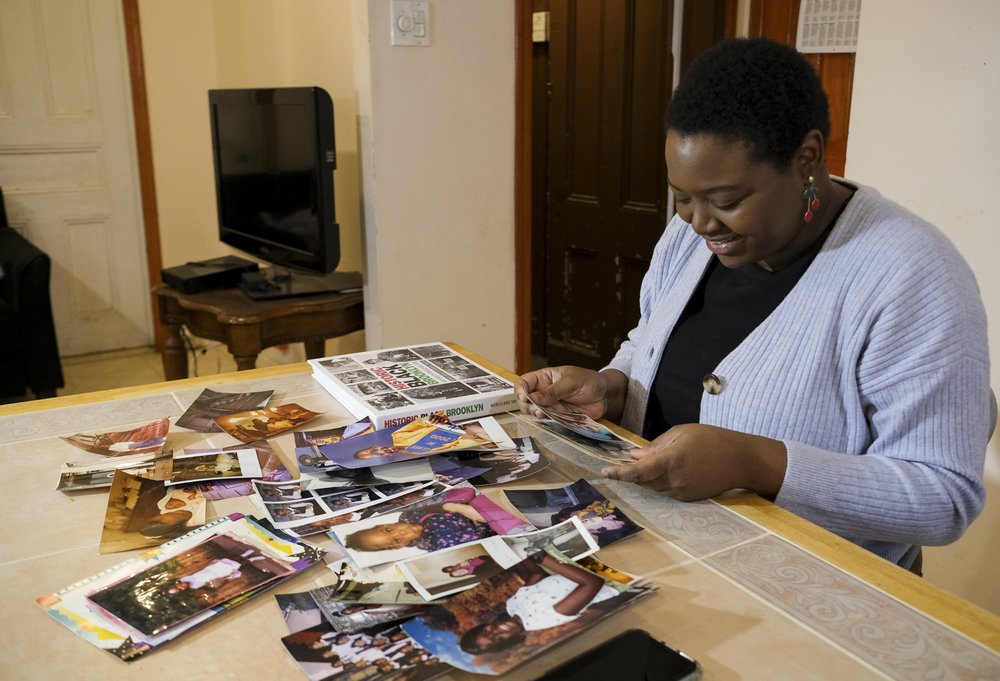 A woman sifts through a large collection of photographs on her kitchen table.