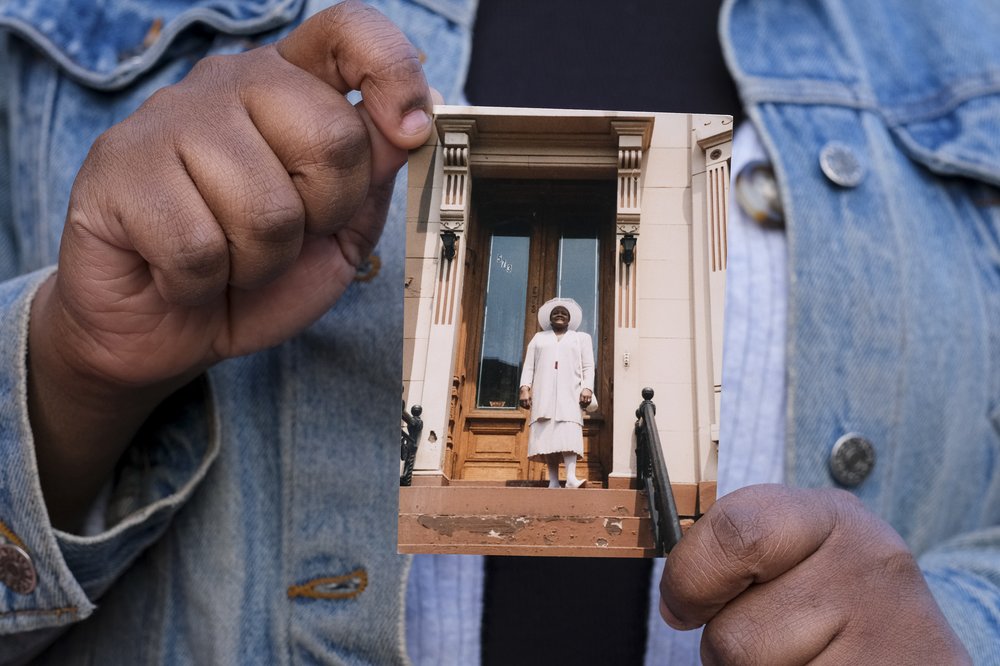 Hands hold a photograph of a woman standing atop brownstone stoop.