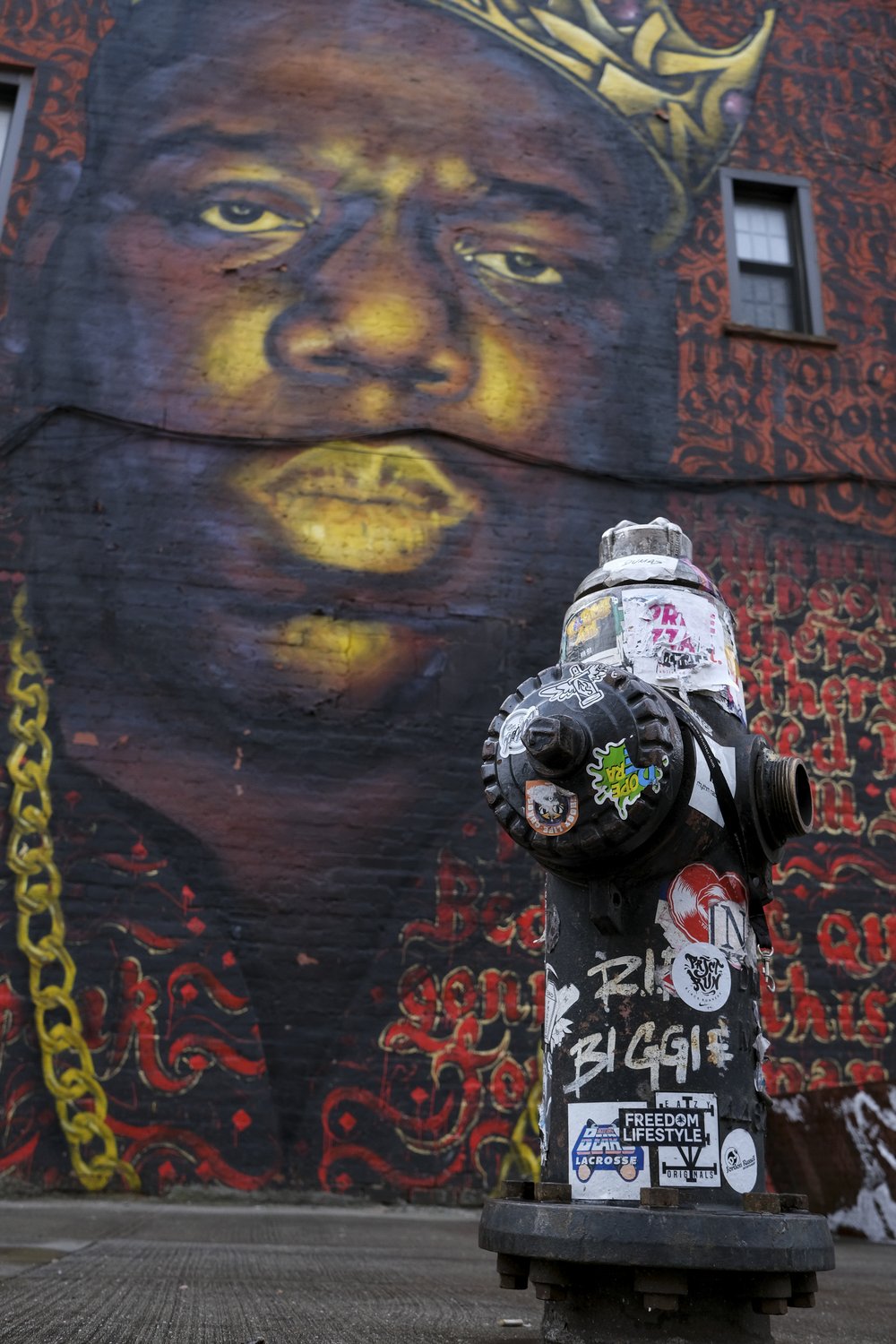 In the foreground, a graffitied fire hydrant that reads, "RIP Biggie." In the background, a large mural of The Notorious B.I.G