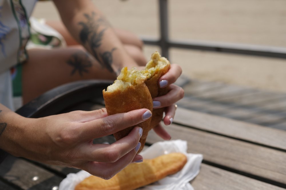 Hands hold a pocket of fried dough filled with meat.
