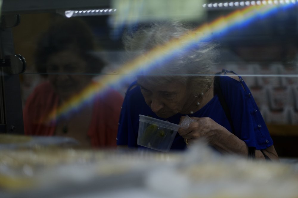 A grey-haired person smells a plastic container of pickles.