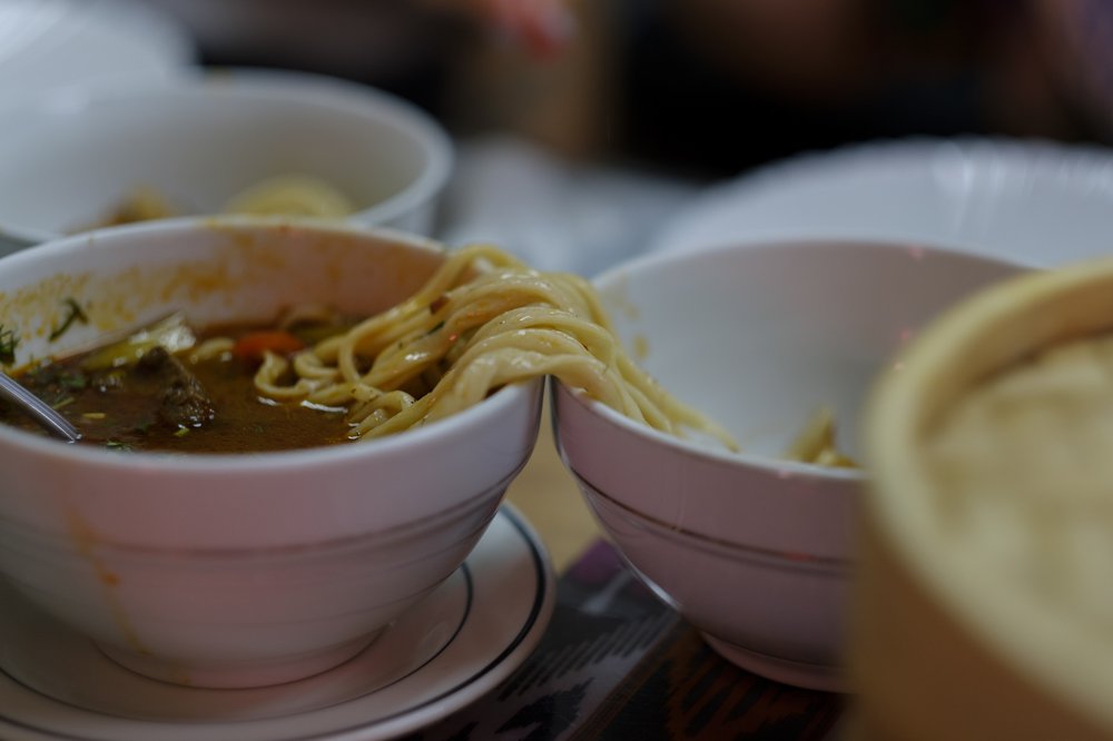 Noodles draped over two bowls. One bowl is filled with a meat soup.