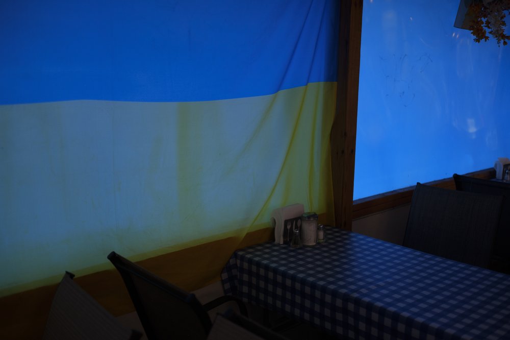 A large Ukrainian flag dims the the light entering a into a restaurant.