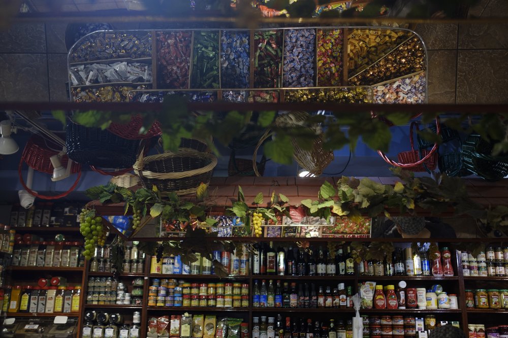 A large selection of spices on a food products sit on a shelf. In a reflection, there is a large while a large tub filled with an assortment of candies.