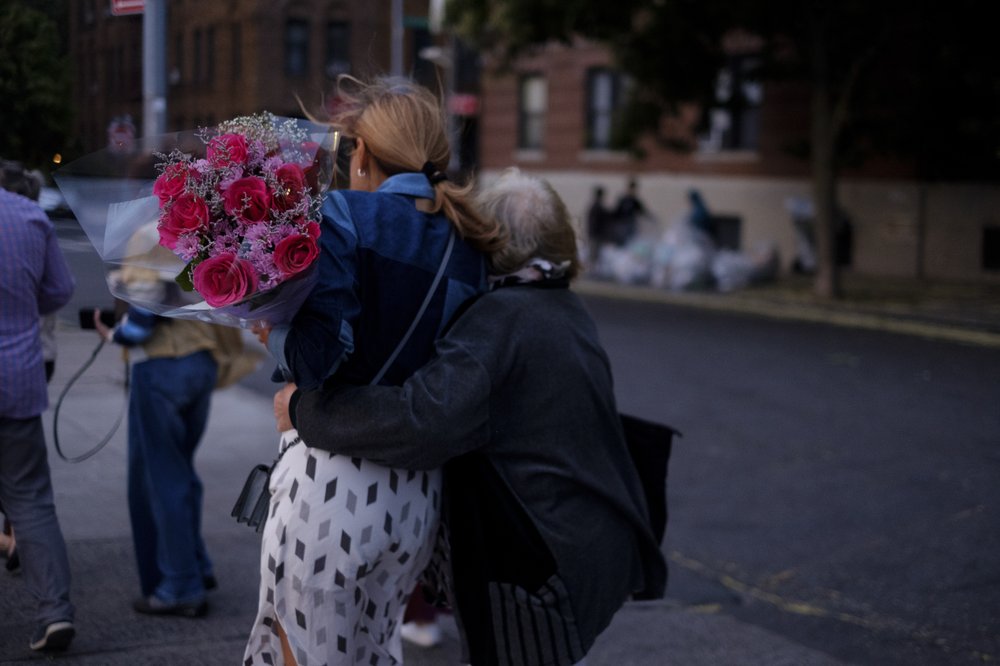 Family members, one holding a bouquet of flowers, embrace while walking.