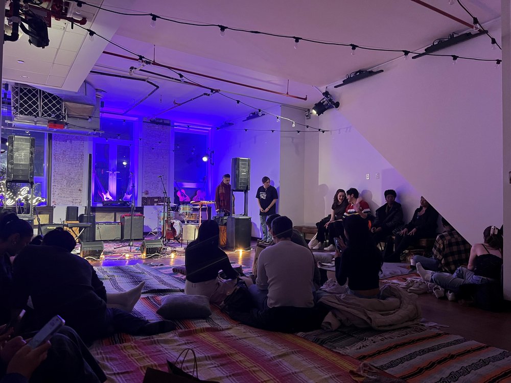 A group of people sitting on a rug preparing to listen to music.
