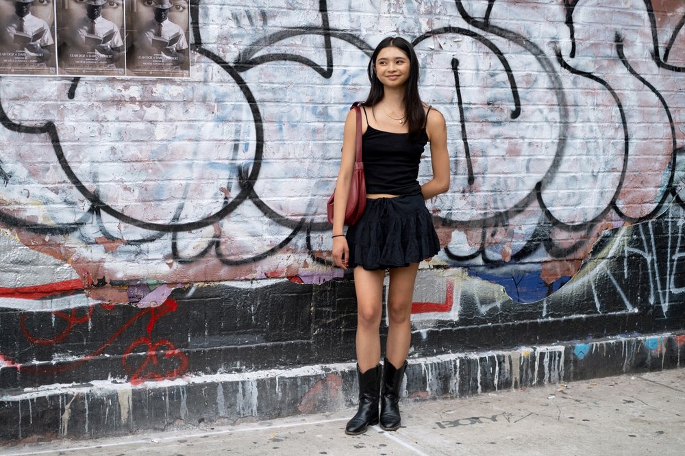 A person wears boots in front of a wall covered in graffiti.
