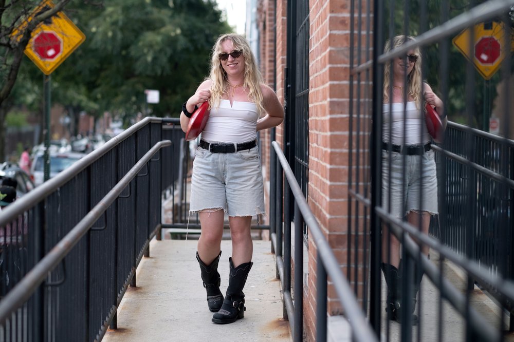 A person stands on a balcony with a white top and denim shorts.
