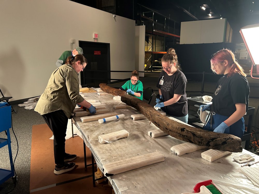 Museum workers tending to a piece of wood.