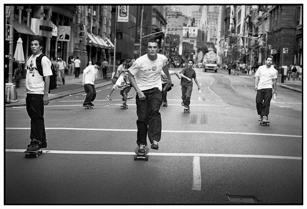 A black and white photo of a several young men on skateboards.