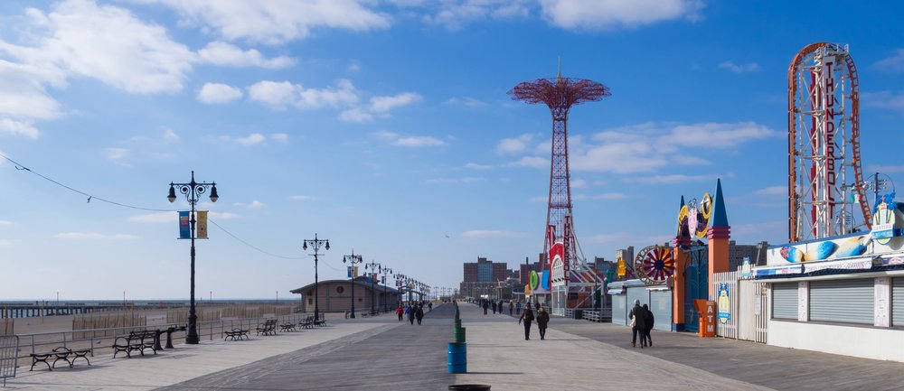 A stock image of the Coney Island boardwalk in the early morning with rides and an empty beach in the background.