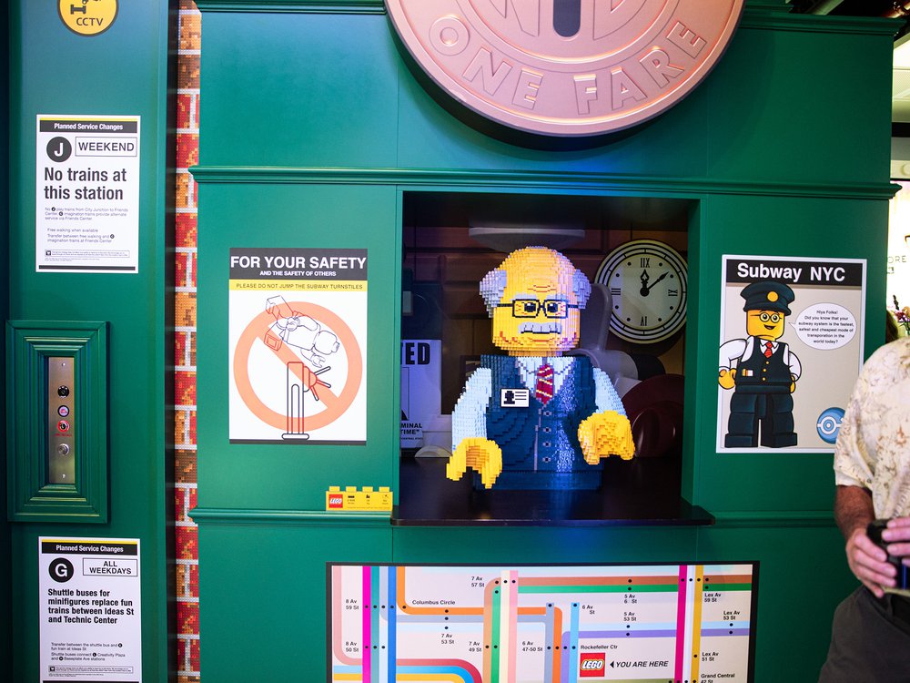 Lego store token booth clerk A Lego sculpture of an MTA employee in an old-fashioned token booth clerk, with the old NYC subway toekn above. There's also a sign that says the J is not working and a subway map of midtown.