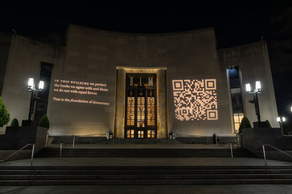 A projected message on the entrance of the Brooklyn Public Library reading "In this building we protect the books we agree with and those we do not with equal fervor. That is the foundation of democracy."