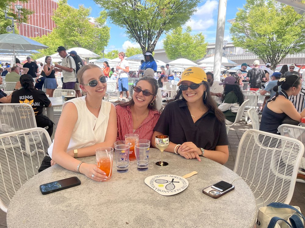 Three women pose at a table with signature US Open cocktails