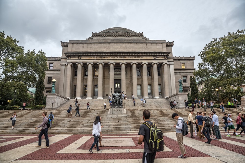 A college campus with buildings, statues, and people.