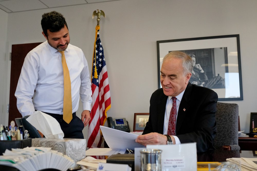 Two men in suits review documents in an office.