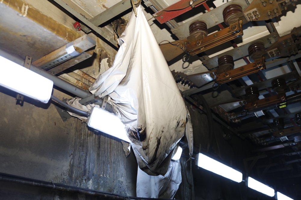 A sheet hanging under a ceiling near heavy duty electrical equipment.