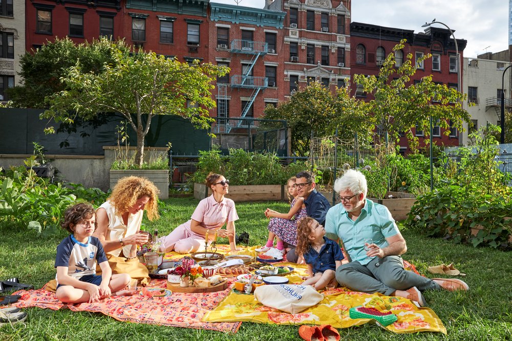 A group of people picnics on a blanket on a lawn.