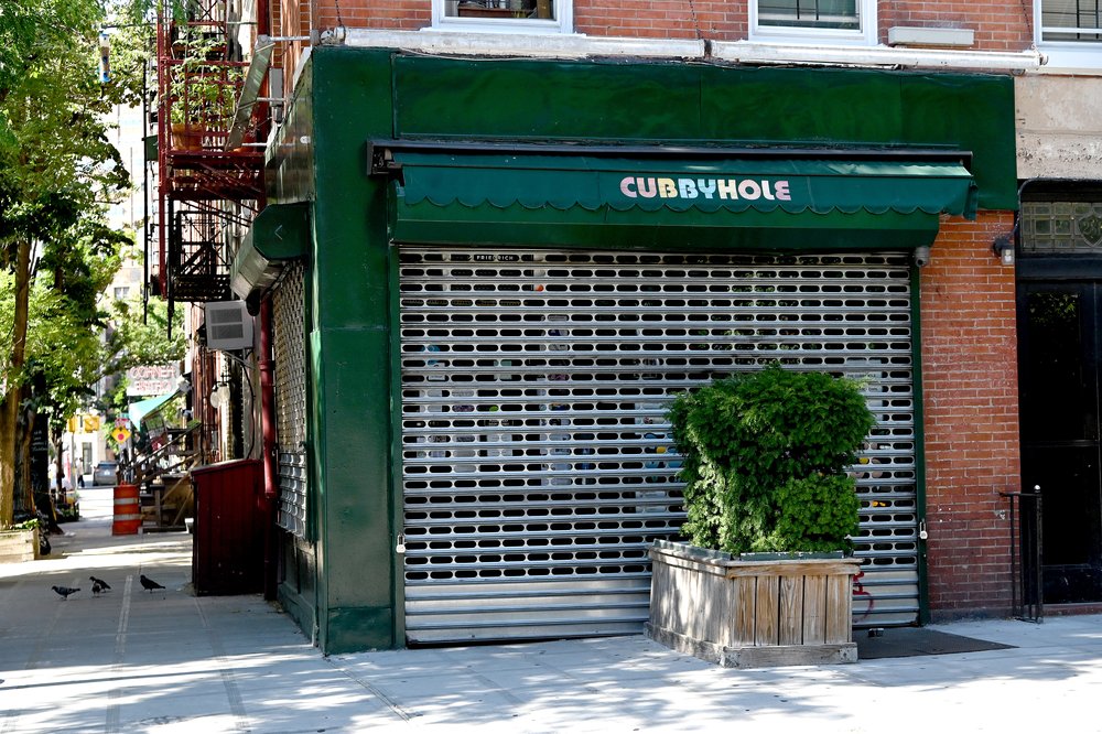 A bar with green awning next to a brick wall on the corner of a New York City street.