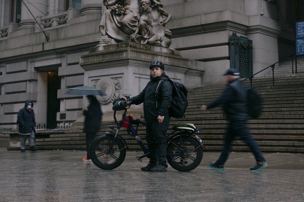 A delivery cyclist stands with e-bike.