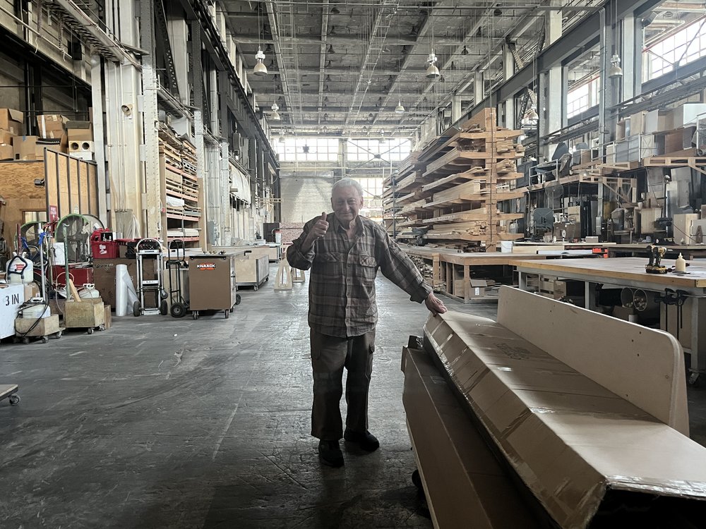 A man stands with his hand on a cardboard box and gives the "thumbs up" sign.