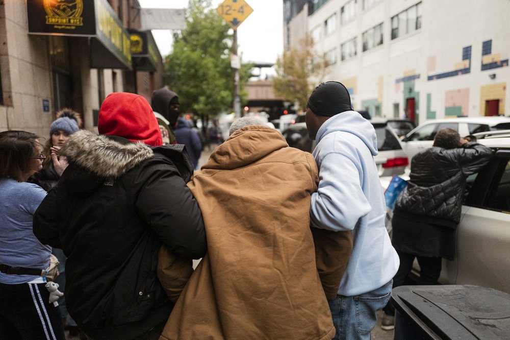 Three men, joined in arms, make their way down a Harlem street.