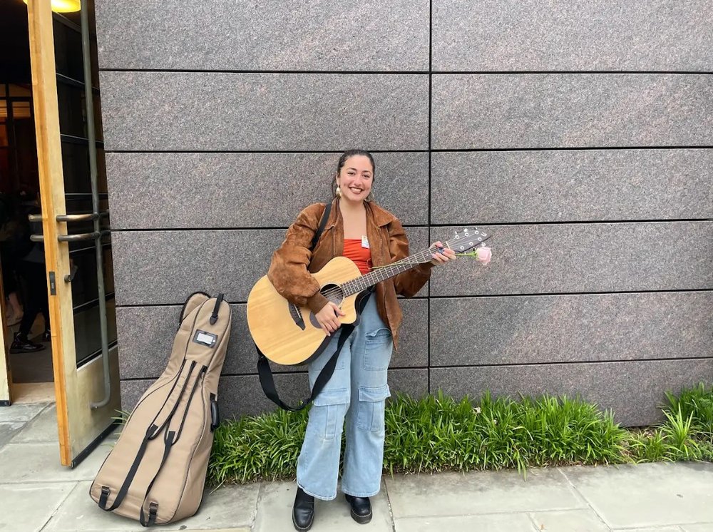 A woman poses in front of a wall holding a guitar.