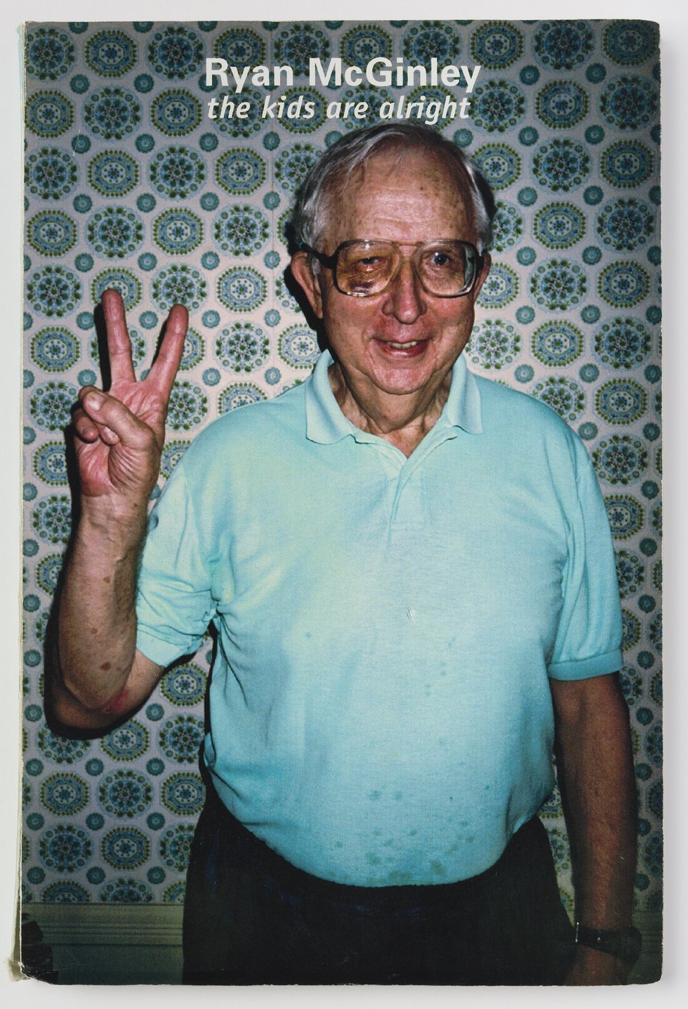 A man in a blue t-shirt holds up two fingers to make the "peace" sign.