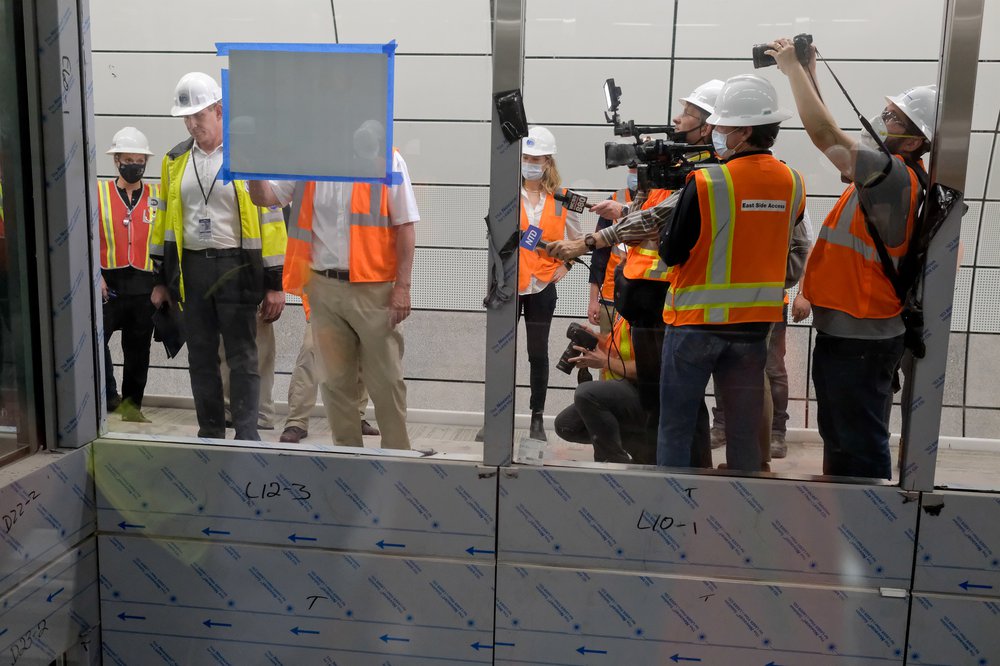 Reporters in orange safety vests and hardhats take photographs