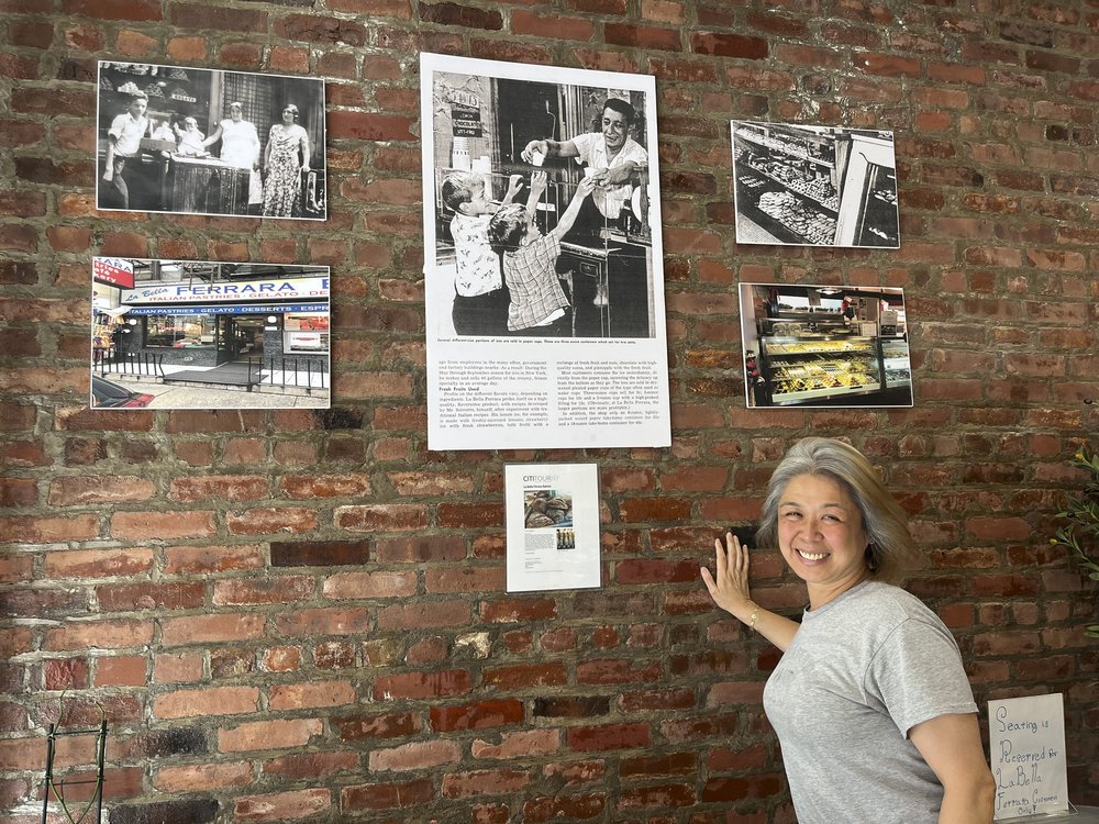 A woman points leans against a brick wall.