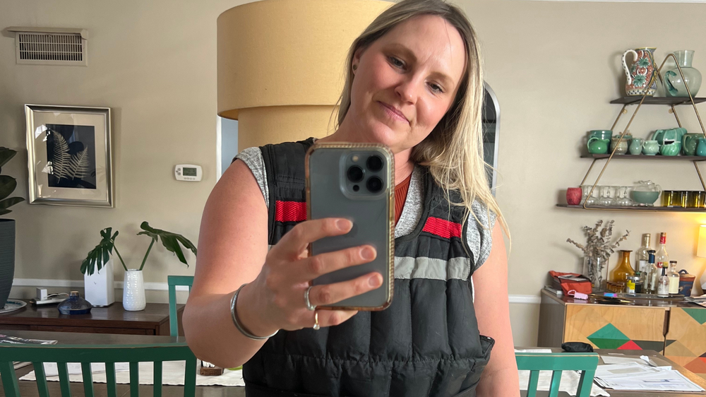 A woman looks in the mirror with a weighted vest.